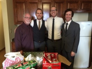 Four men standing in a kitchen next to some boxes of soda.